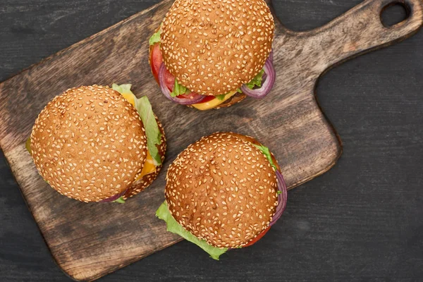 Top view of delicious fresh burgers on cutting board on black wooden table — Stock Photo