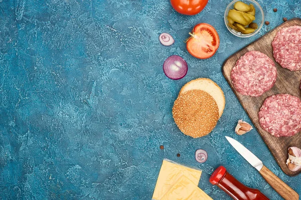 Vue de dessus des ingrédients du cheeseburger frais sur une surface texturée bleue — Photo de stock