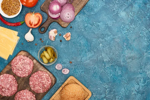 Vista superior de ingredientes de hambúrguer fresco na superfície texturizada azul com espaço de cópia — Fotografia de Stock