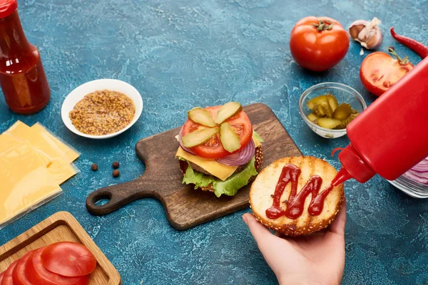 Vista recortada de la mujer cocinar deliciosa hamburguesa fresca en la superficie de textura azul - foto de stock