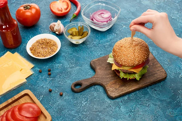 Vista recortada de la mujer cocinar deliciosa hamburguesa fresca en la superficie de textura azul - foto de stock
