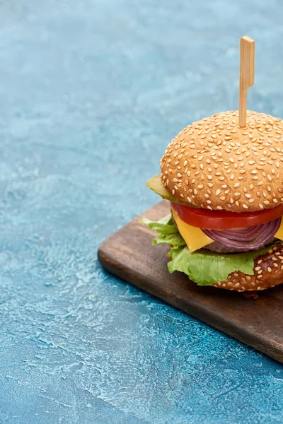 Delicious cheeseburger on wooden board on blue textured surface — Stock Photo
