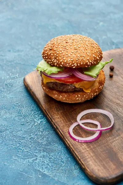 Delicious cheeseburger on wooden board on blue textured surface — Stock Photo