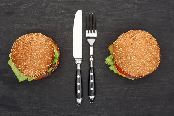 Tasty fresh burgers on wooden black table with cutlery — Stock Photo