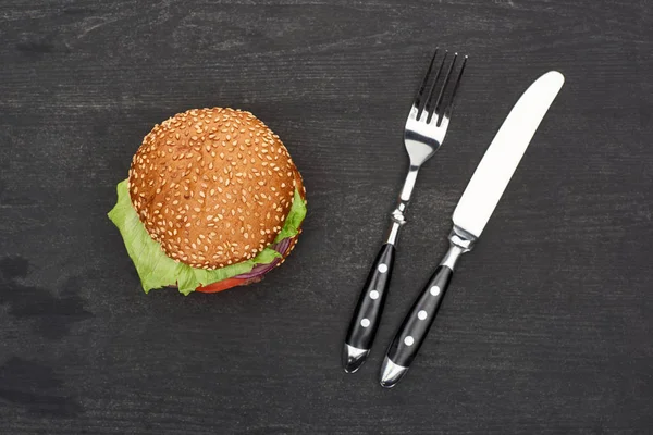 Tasty fresh burger on wooden black table with cutlery — Stock Photo