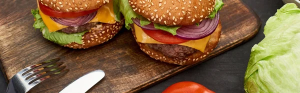 Tasty fresh cheeseburgers on wooden board with cutlery, panoramic shot — Stock Photo