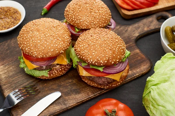 Sabrosas hamburguesas con queso fresco sobre tabla de madera con cubiertos - foto de stock