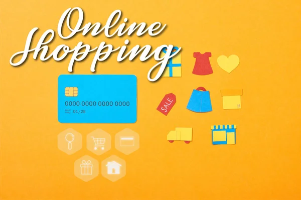 Pose plate avec modèle de carte de crédit bleue près des icônes de shopping isolé sur orange avec illustration de magasinage en ligne — Photo de stock