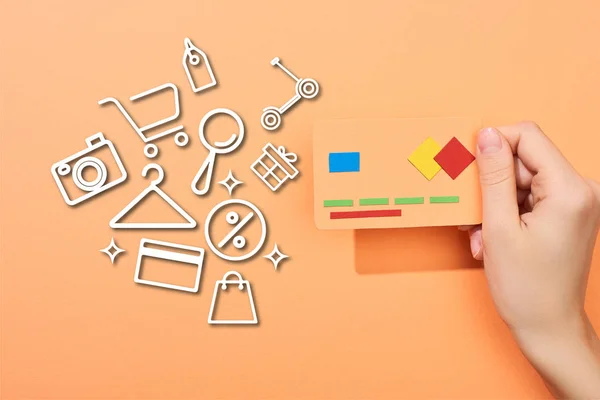 Cropped view of woman holding credit card template on peach background with icons illustration — Stock Photo