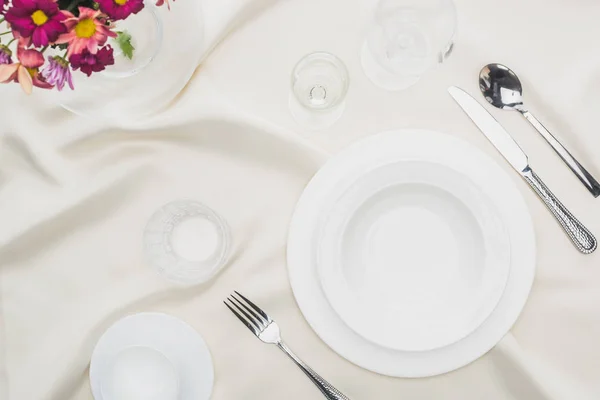 Vue de dessus de vaisselle avec verres, tasse à café et bouquet sur nappe blanche — Photo de stock