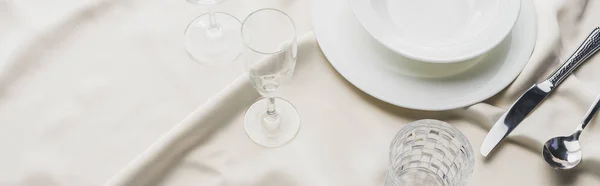 High angle view of dinnerware with cutlery and glasses on white tablecloth, panoramic shot — Stock Photo