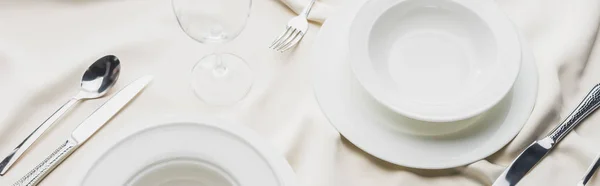 Panorâmica tiro de servir utensílios de mesa com copo de vinho na toalha de mesa branca — Fotografia de Stock