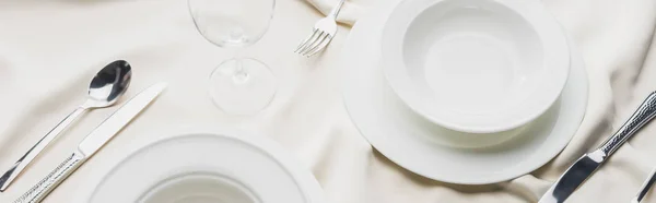 Vue panoramique de la vaisselle de service avec verre à vin sur la nappe blanche — Photo de stock