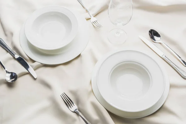 High angle view of dinnerware with cutlery and wine glass on wavy tablecloth — Stock Photo