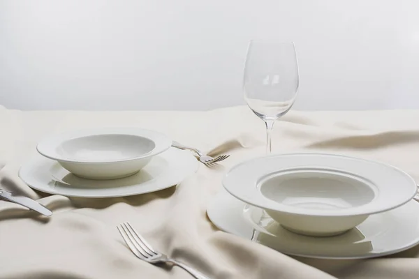 Plates with cutlery and clear wine glass on white tablecloth on grey background — Stock Photo