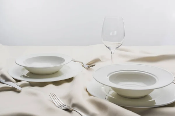 Assiettes avec couverts et verre à vin transparent sur nappe blanche sur fond gris — Photo de stock