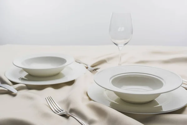 Selective focus of dinnerware and empty wine glass on tablecloth on grey background — Stock Photo