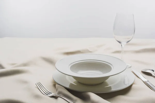 Selective focus of plates and wine glass on tablecloth on grey background — Stock Photo