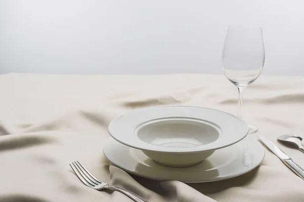 Selective focus of plates and wine glass on tablecloth on grey background — Stock Photo