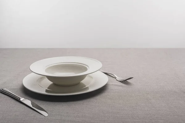 Placas com garfo e faca na toalha de mesa em fundo cinza — Fotografia de Stock