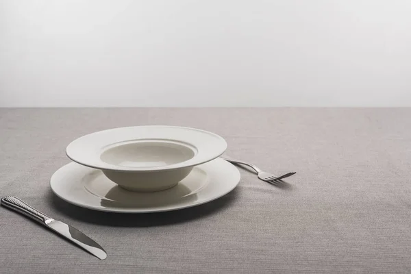 Plates with fork and knife on tablecloth on grey background — Stock Photo