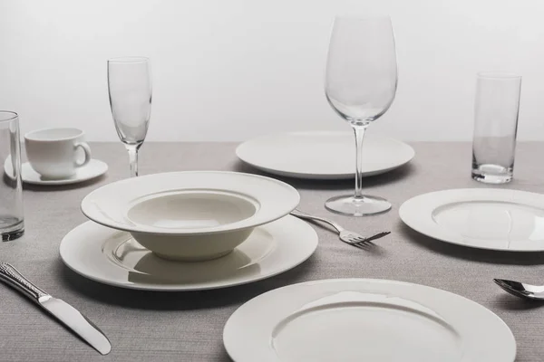 Dishware and transparent glasses on tablecloth on grey background — Stock Photo