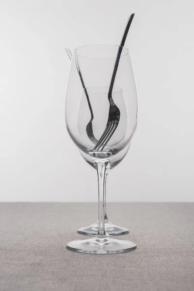 Selective focus of forks in clear wine glasses on tablecloth isolated on grey — Stock Photo