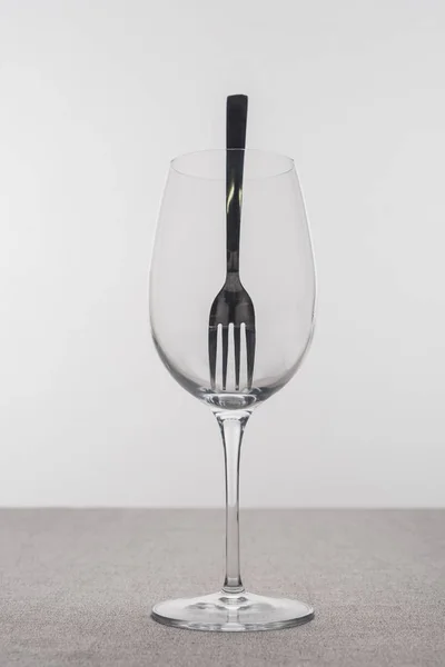 Fork in transparent wine glass on tablecloth isolated on grey — Stock Photo