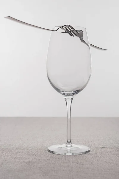 Tenedores en copa de vino vacía en mantel aislado en gris - foto de stock
