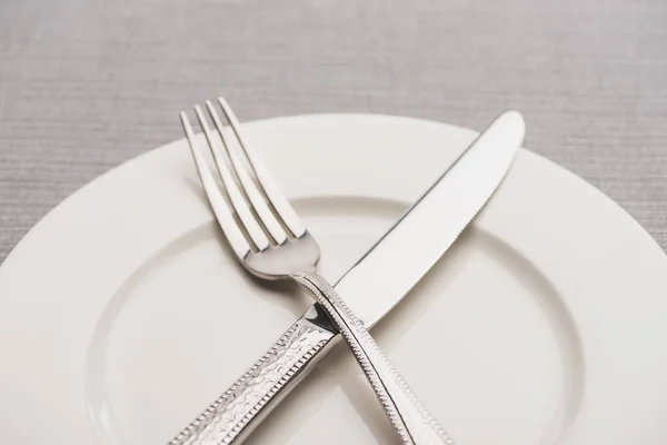 Close up view of fork and knife on empty plate on grey surface — Stock Photo