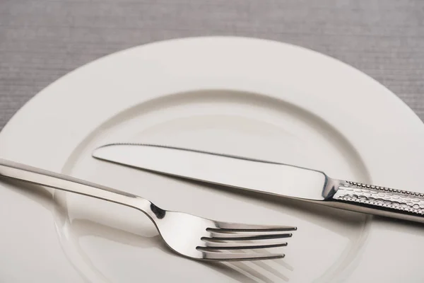 Close up view of cutlery on empty plate on grey surface — Stock Photo