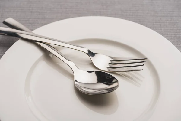 Close up view of shiny spoon and fork on plate on grey surface — Stock Photo