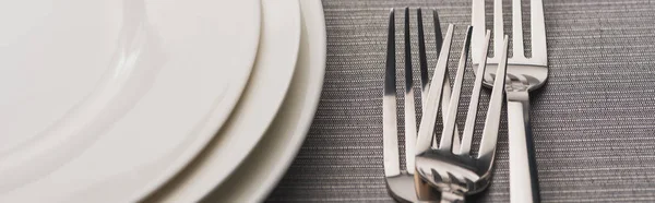 Panoramic shot of forks beside empty plates on grey surface — Stock Photo