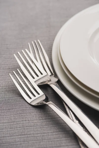 Блестящие вилки рядом с подачей тарелок на серой скатерти — стоковое фото