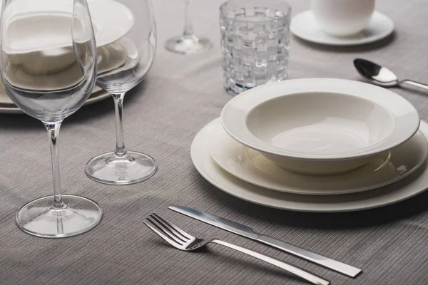 Serving dinnerware with cutlery and glasses on grey linen tablecloth — Stock Photo