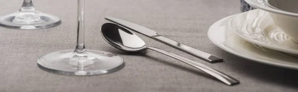 Cucchiaio e forchetta accanto a bicchieri e piatti su stoffa grigia, colpo panoramico — Foto stock