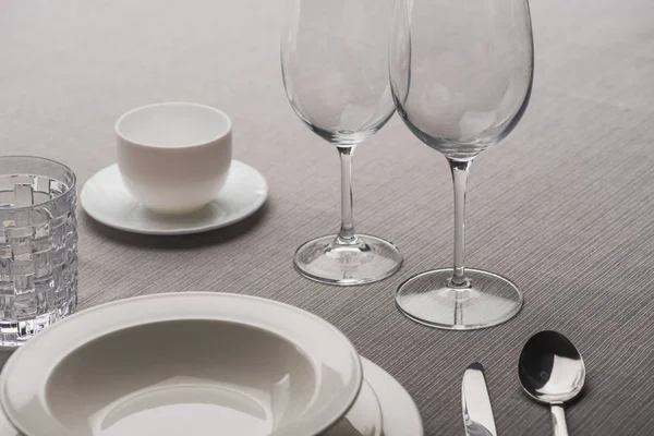 Clear wine glasses beside dishware and coffee cup on grey cloth — Stock Photo