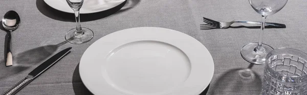 Panoramic shot of serving tableware with glasses on grey cloth — Stock Photo