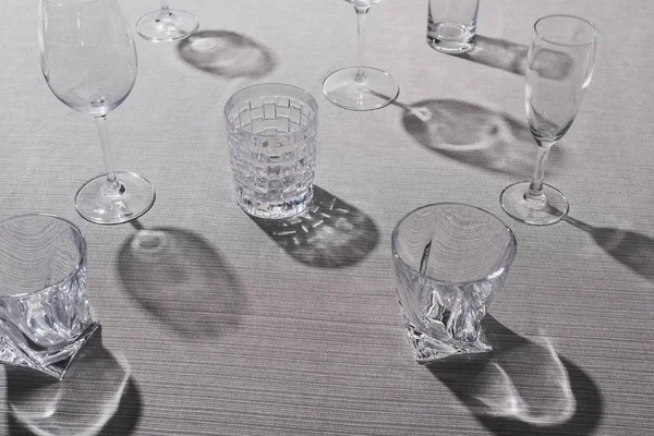 High angle view of transparent glasses with shadow on grey tablecloth — Stock Photo