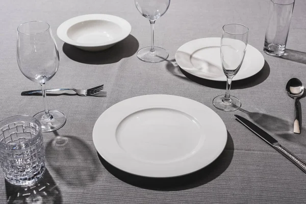 Empty serving tableware with glasses on grey cloth — Stock Photo
