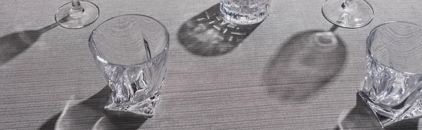 Panoramic shot of clear glasses with shadow on grey cloth — Stock Photo