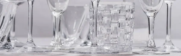Foto panorámica de vasos claros sobre mantel sobre fondo gris - foto de stock