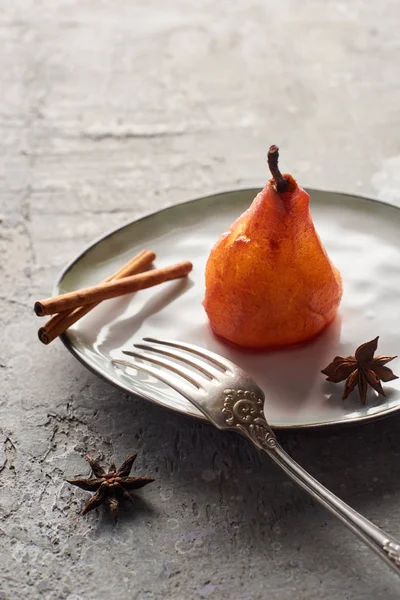 Delicious pear in wine with cinnamon and anise on plate with silver fork on grey concrete surface — Stock Photo