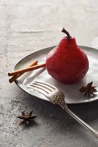 Deliziosa pera in vino con cannella e anice su piatto con forchetta argento su superficie in cemento grigio — Foto stock