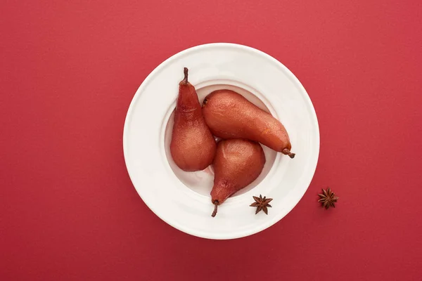 Vista superior de la deliciosa pera en vino con anís en el plato sobre fondo rojo - foto de stock