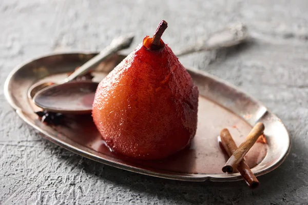 Delicioso pera en vino con canela en plato con cucharas de plata en la superficie de hormigón gris - foto de stock