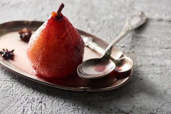 Delicious pear in wine with anise on plate with silver spoons on grey concrete surface — Stock Photo