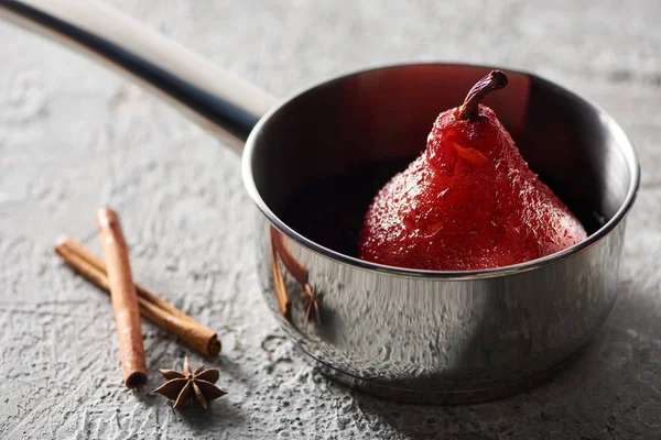 Selective focus of delicious pear in wine in stewpan near cinnamon and anise on grey concrete surface — Stock Photo