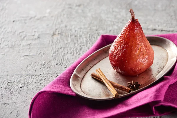 Delicious pear in wine with cinnamon and anise on silver plate near pink napkin on grey concrete surface — Stock Photo