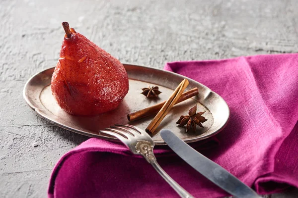 Deliciosa pêra no vinho com canela e anis na placa de prata na superfície de concreto cinza com guardanapo rosa, faca e garfo — Fotografia de Stock